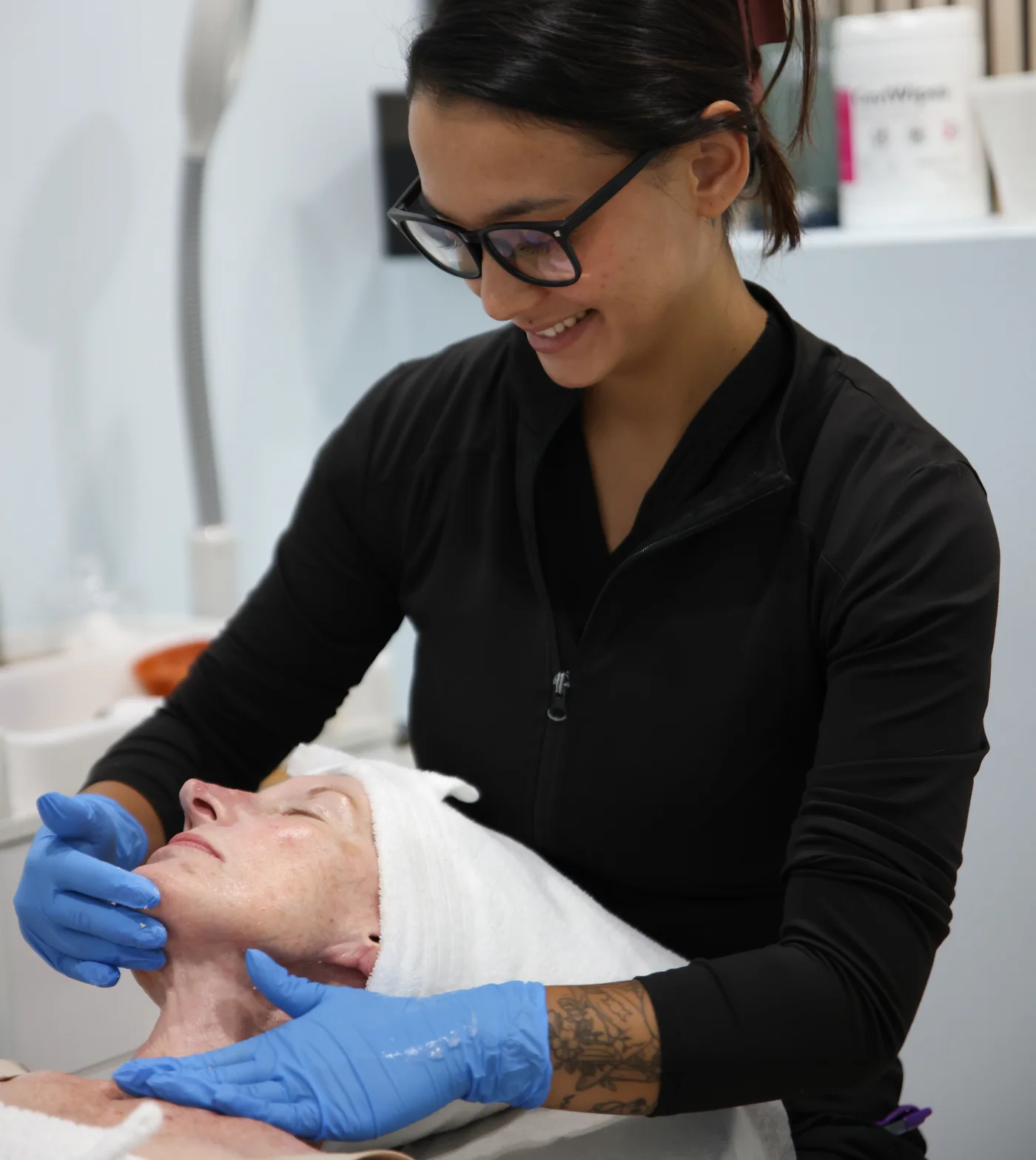 A Mirror Esthetics esthetician smiling as she works on a client during a facial treatment