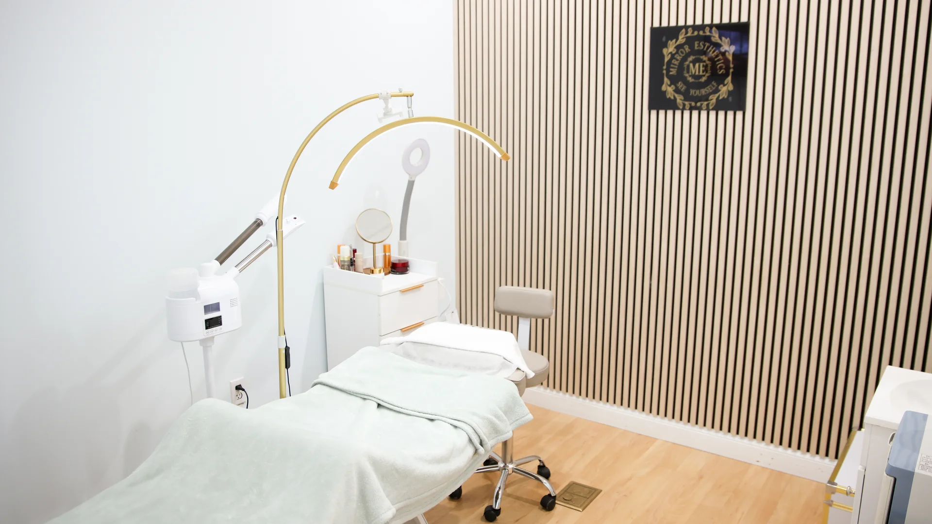 A Mirror Esthetics treatment room with the facial bed, LED arc light and wood slat wall