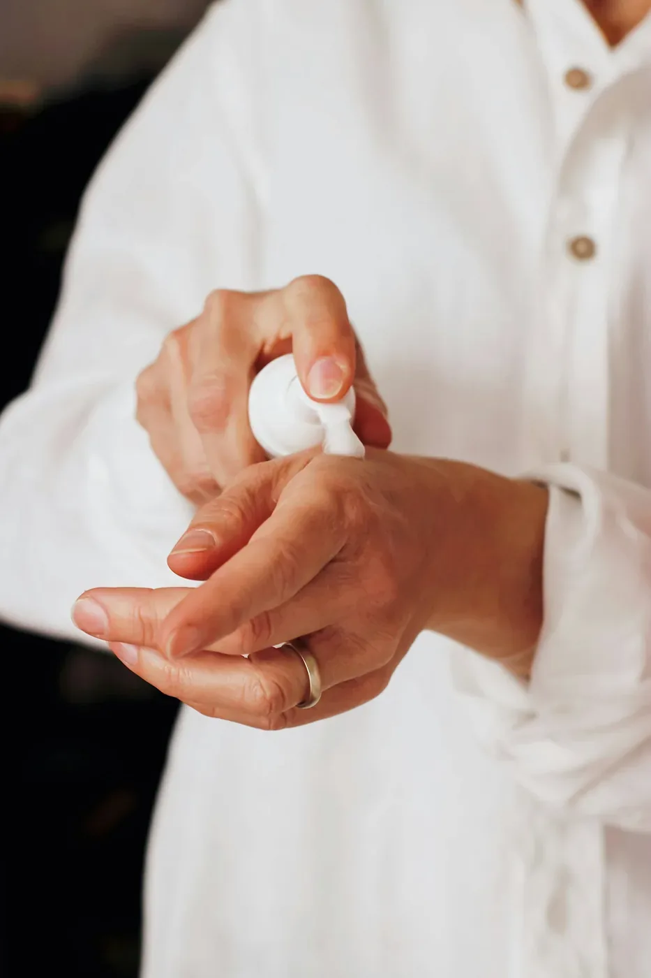 Hands dispensing a skincare product from a white pump bottle.