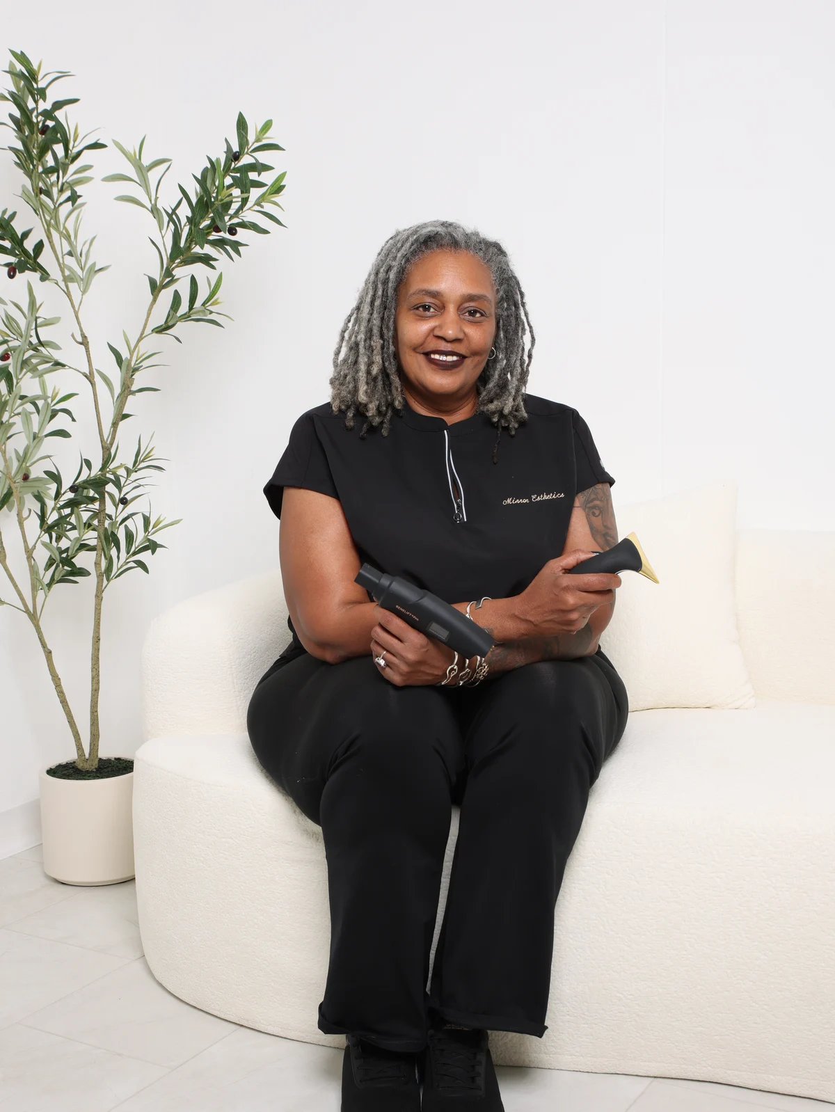 A Mirror Esthetics esthetician seated in the studio lounge, holding a skin treatment device